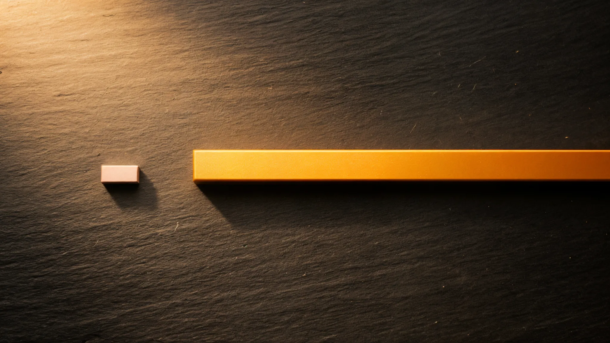 Two horizontal metal bars on dark slate: one tiny pale bar and one long orange-gold bar showing dramatic size contrast